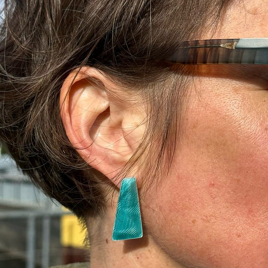 Close-up of a petrol enamel trapezoid stud earring worn on the ear
