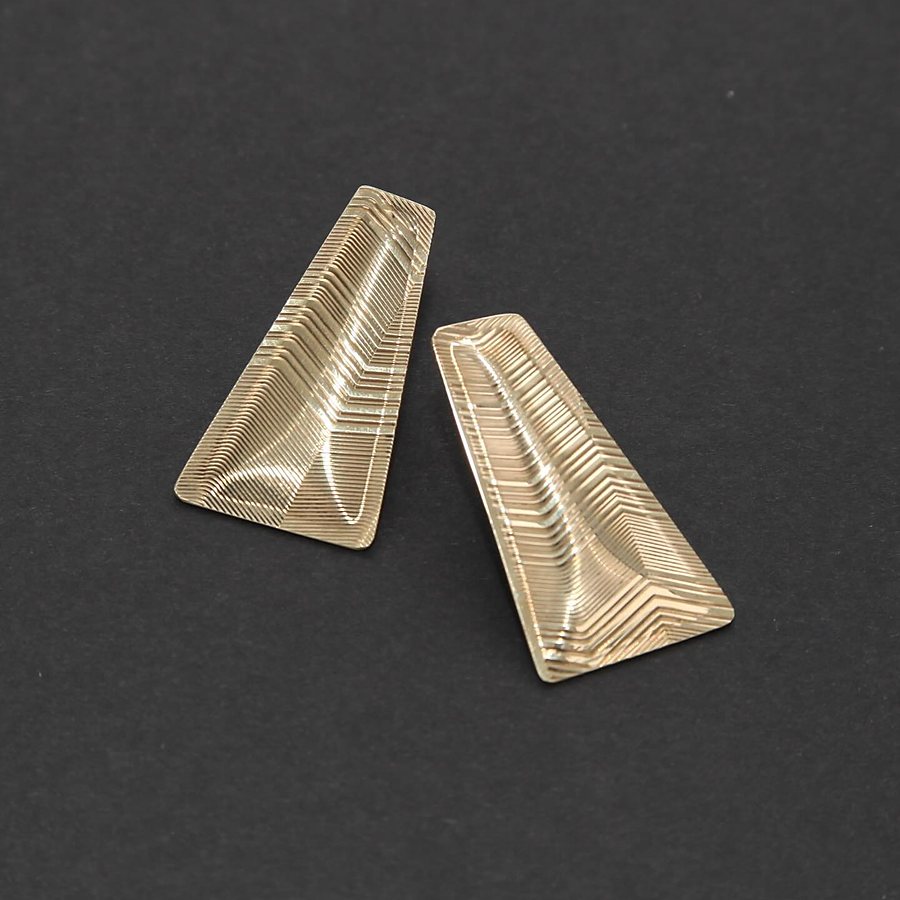 Pair of brass trapezoid stud earrings with guilloché lines on a dark background