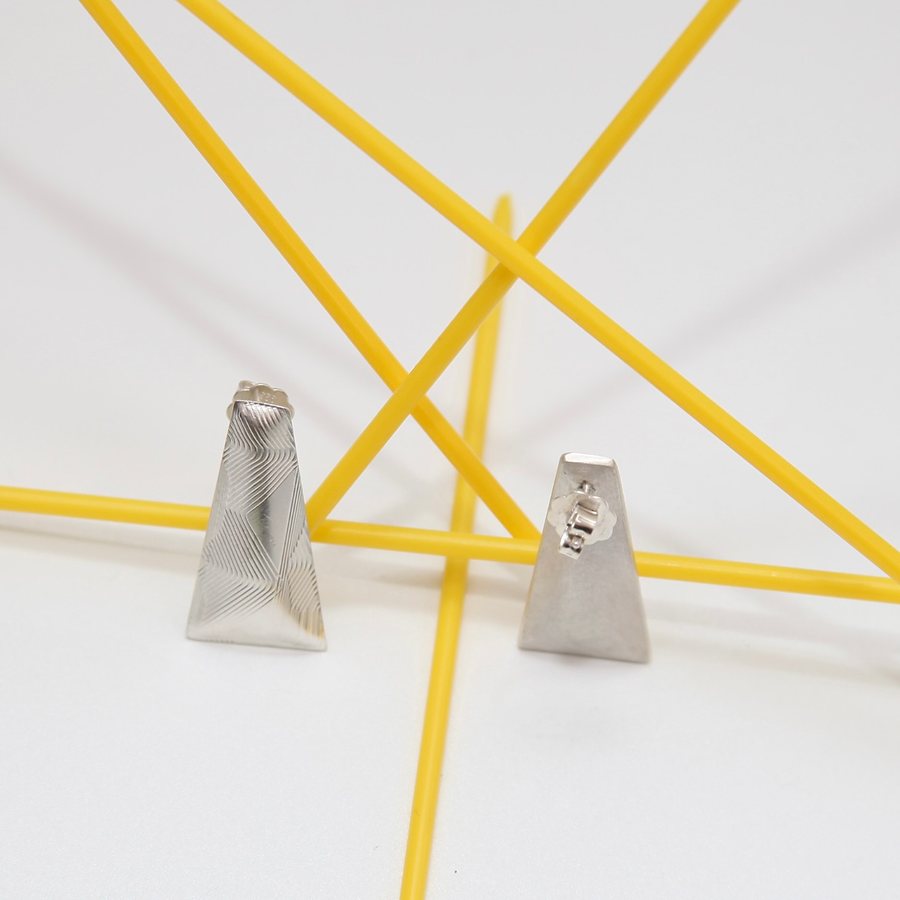 Silver trapezoid stud earrings, one showing its back with the post
